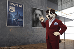 Person in a red suit with a bear mascot head standing in a room with posters on the wall.